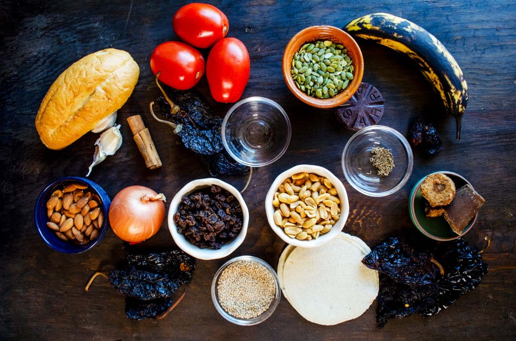 Ingredientes tradicionales del mole poblano: chiles, tomates, chocolate, nueces y semillas sobre mesa de madera